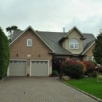 image of a large suburban house with double car garage, manicured lawn, and large garden, new roof installed by Baron Roofing & Siding