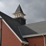image of a church with stained glass windows, a tall steeple, and a newly-installed roof, installed by Baron Roofing & Siding in Fonthill